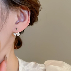 Close-up of sparkling zircon bow earrings with silver finish worn on model's ear
