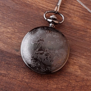 Detail of vintage black alloy pocket watch with intricate floral engraving on wooden surface