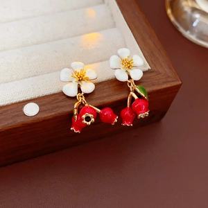 Detail of vintage enamel earrings with white flower and red fruit pendants on wood box