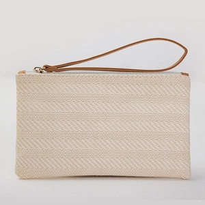 Detailed view of the woven texture and dark brown leather wristlet strap on a cream bag