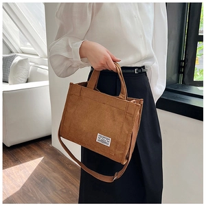 Detail of brown corduroy tote bag featuring adjustable strap and white brand label