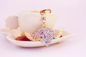 Close-up of golden heart keychain with colorful rhinestones and angel wings detail
