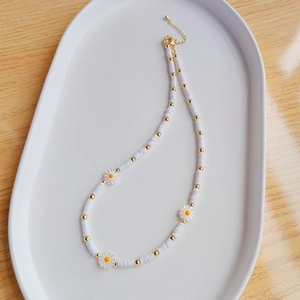 Detail of beaded daisy necklace with white shells and gold metal clasp on a tray