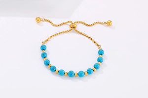 Détail du bracelet en acier doré avec perles turquoise et fermoir coulissant réglable
