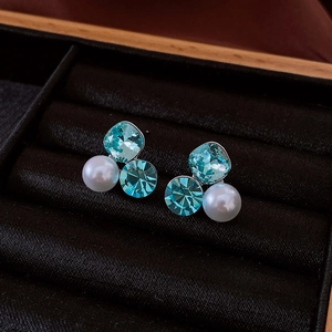 Detailed cluster of blue crystals and white pearl earrings on black velvet padding