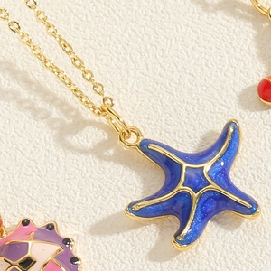 Macro shot of blue enamel starfish pendant with gold chain on textured background