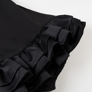 Detailed view of black satin ruffles and layered pleats on a backless mini dress