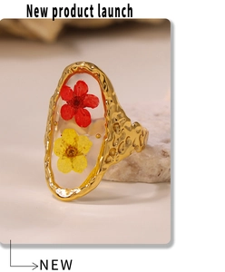 Detail of gold hammered ring featuring a clear resin oval with red and yellow dried flowers