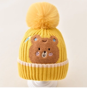 Close-up of yellow knit baby hat with soft pom-pom and cute brown bear embroidery