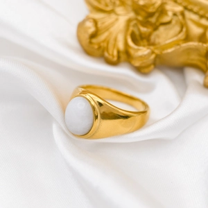 Macro detail of 18k gold plated signet ring with white agate gemstone on white silk