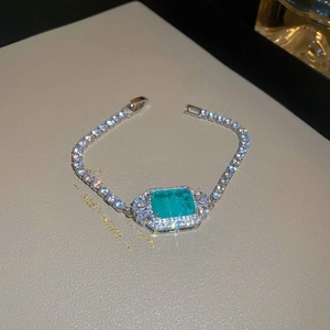 Detail of silver luxury bracelet with emerald-cut green stone and sparkling zircon halo