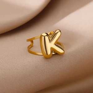 Macro view of gold plated bubble letter K ring on satin background with hollow band
