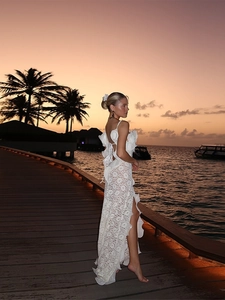 Détail d'une robe longue en dentelle dos nu avec volants et fente haute sur la plage