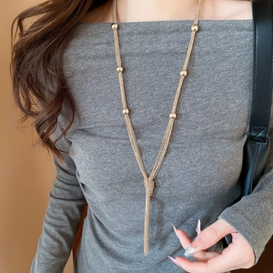 Detail of long gold layered tassel necklace with metallic beads on model's sweater