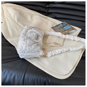 Close-up of white ruched cloud bag with metal chain on a beige blazer background