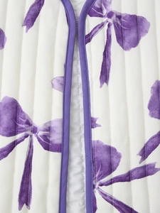 Close-up of quilted cotton jacket fabric featuring purple bow print and piped edges