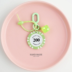 Detail of green poker chip and translucent dice keychain on a pink display tray