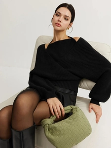 Detail of a chic black cross-front knit sweater styled with a green woven handbag