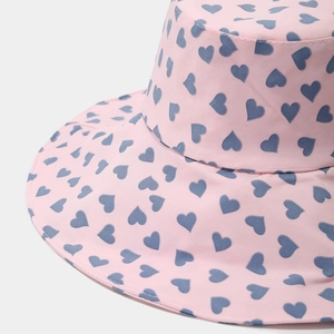 Close-up of pink bucket hat featuring blue heart patterns and cotton twill texture