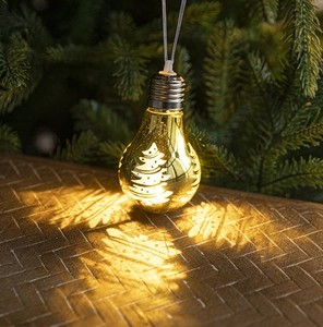 Detail of gold LED Christmas ornament projecting a warm tree shadow on a wooden surface