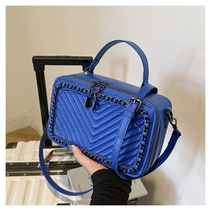 Detail of blue V-quilted handbag featuring dark chain trim and dual zipper closure