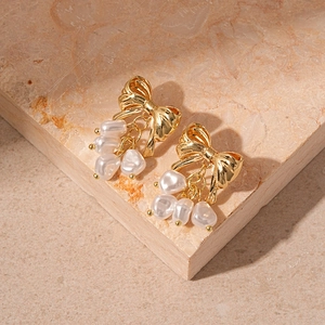 Detailed view of gold bow earrings with three dangling baroque pearls on stone