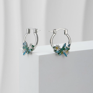 Macro view of silver hoop earrings featuring blue dragonfly and daisy enamel charms