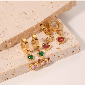Macro shot of gold-plated heart-shaped zircon earrings with green and pink gemstones