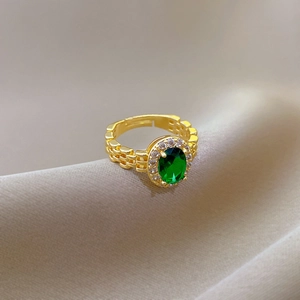 Detail of gold watchband ring featuring a green emerald oval stone and pavé accents
