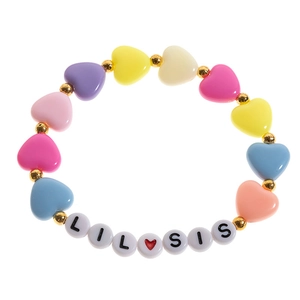 Macro detail of acrylic heart beads with Lil Sis letter charms on a colorful bracelet
