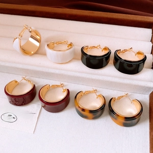 Close-up of four colors of C-shaped resin and gold earrings in a jewelry box