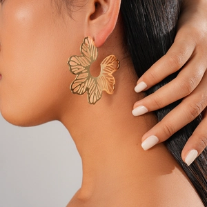 Detail shot of a model wearing a large golden hollow floral earring with a metallic finish