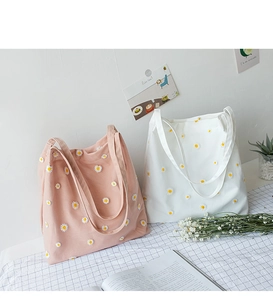 Close-up of pink and white canvas tote bags with delicate daisy embroidery on grid background