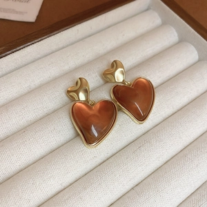Detail of amber resin heart earrings with gold metal edges on a cream velvet tray