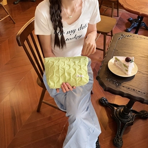 Close-up of light green quilted pouch texture with a colorful woven logo on a wooden table