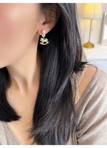 Close-up of elegant gold rocking horse earrings with pearls worn by a model