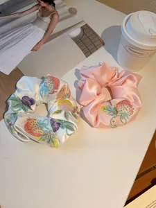 Satin scrunchies with strawberry embroidery shown with coffee cup and magazine