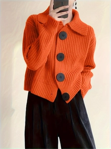 Detail of bright orange knitted cardigan with large black buttons in a casual loose fit