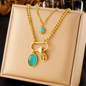 Detail of gold double chain necklace featuring green gemstone and tree of life charms