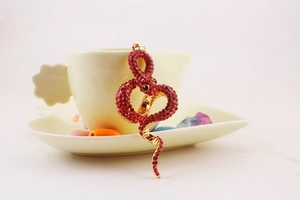 Close-up of golden snake pendant with red rhinestones on a tea saucer display
