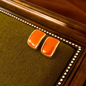 Detailed close-up of vintage orange enamel square stud earrings on dark green fabric