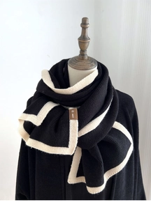 Detail of black knit scarf with white trim and brown leather tag on a mannequin