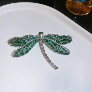 Detailweergave van een luxe libellenbroche met smaragdgroene zirkoon op een wit bord