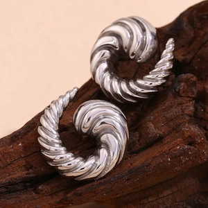 Macro view of silver whirlwind spiral earrings with textured finish on wood base