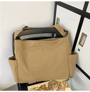 Detail of khaki canvas tote bag hanging on a chair showing the side pocket and texture