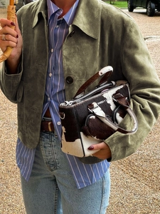 Close-up of cow print textured handbag with brand logo and green autumn jacket