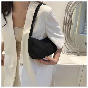 Fashionable black corduroy baguette bag worn under the arm with a white blazer