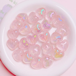 Macro shot of shimmering pink heart-shaped beads in a white dish for DIY jewelry