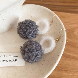 Dettaglio di orecchini di peluche grigi e bianchi su piatto di ceramica e legno