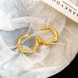 Detail view of twisted gold C-shape hoop earrings with crystal pavé and textured finish